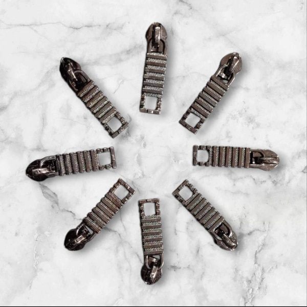 Fancy zipper sliders feature decorative designs and unique finishes, adding a stylish element to bags and garments. They often include:Materials: Typically made from metal or high-quality plastic, sometimes with added embellishments like gems or colored coatings.Shapes: Available in various shapes, including ornate designs, themed motifs, or custom logos.Finishes: Can come in polished, matte, or textured finishes, enhancing visual appeal.Functionality: While primarily decorative, they retain the functionality of standard sliders, providing smooth operation.Applications: Commonly found in fashion bags, upscale apparel, and accessories where aesthetics are key.If you need specific examples or styles, let me know!ChatGPT can make mistakes. Check important info.