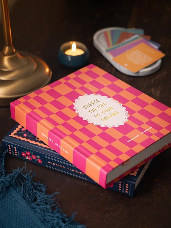 Our annual undated planner is thoughtfully designed to help you live your best life. With its undated layout, you can start planning whenever you're ready, allowing you to set your own pace for the days, weeks and months ahead. Track your mental well-being, productivity, personal life, and physical health with dedicated worksheets for different aspects of life. Use it to set goals, track progress, and celebrate your achievements. Inspired by the vibrant colours of nature and the objects around us that often go unnoticed, every detail of this planner is like a breath of fresh air for your desk. With its colorful pages and uplifting quotes, you'll feel motivated to take action and create the life you desire.The planner comes in a luxurious hardbound box along with 5 thoughtful freebies:A pocket notebook to jot down everything on the goSet of 50 Journaling Prompt cards for guided journalingA notepad for your daily listsSet of 3 greeting cardsA Canvas pouch to hold all your essentials together12 open-dated monthly plan layouts52 weekly layouts with 2 dates per pageThoughtful activities to do each weekWeekly reflection pages for self-assessmentYear-at-a-glance overviewGoal setting pages to visualize your dreamsVision board, to create your ideal futureSelf-care assessment pages, for holistic well-beingHabit trackerFinance trackerMotivating illustrations and quotes2 ribbon bookmarks, each for a month and a weekAdditional notes pages for jotting down ideasBack pocket for keeping loose papers150+ StickersPLUS 5 FREEBIES!Details:Size: 17.5 x 21 x 3 cmsPages: 352 pages of 100 GSM Natural Shade PaperCover: Hardbound matt laminated with gold foil accentsBox: Hardbound with gold foil accents