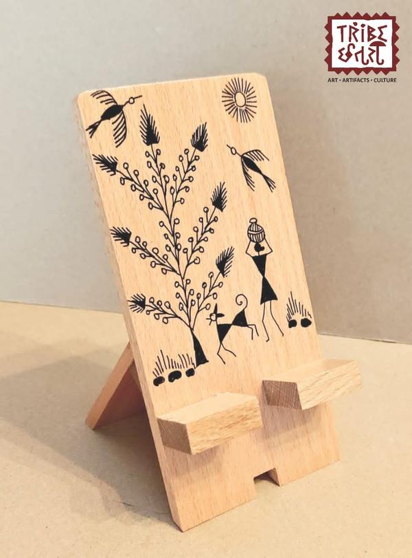 A Wooden Warli Painted Mobile Stand typically refers to a handcrafted wooden stand for holding a mobile phone, decorated with Warli art — a traditional tribal art form from Maharashtra, India. Warli art features simple, white geometric patterns like circles, triangles, and lines on a contrasting background, often depicting scenes of rural life, nature, or tribal rituals.Tribe Chatari in Pune offers a selection of Warli-themed office stationery that beautifully blends traditional tribal art with functional design. Their collection includes handcrafted items such as pen stand & tea coasters etc.