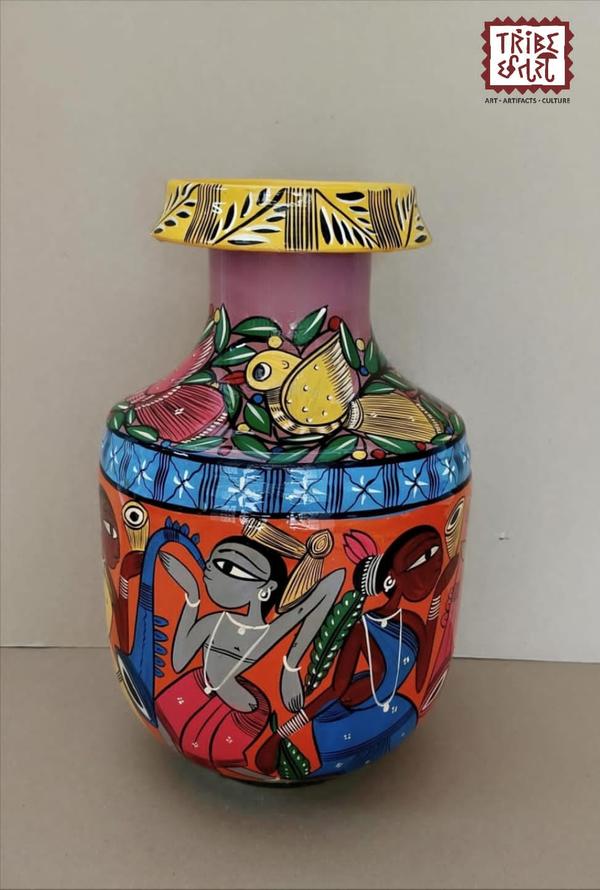Santhali Hand-Painted Metal Pots These hand-painted metal pots feature the vibrant and earthy Santhal painting style, a traditional tribal art form from the Santhal community of West Bengal.🎨 Art Style:Santhal paintings are known for their bold lines, rhythmic patterns, and vibrant storytelling.Common themes include tribal dances, music, nature, daily village life, and scenes of community bonding.The art reflects the joyous spirit and close connection to nature of the Santhal people.🖌️ Craftsmanship:Each pot is individually hand-painted by rural artisans. The figures are often depicted in motion dancing, playing instruments, or farming — giving the artwork a dynamic and lively character.🌿 Cultural Value:These pots celebrate tribal heritage and indigenous identity, making them not just decorative items but also narratives of a living culture.Perfect for ethnic décor, gifting, or cultural collections.Available at Tribe Chatari, these pots are one-of-a-kind pieces that carry the spirit of rural Bengal into your living space.Size--5x11