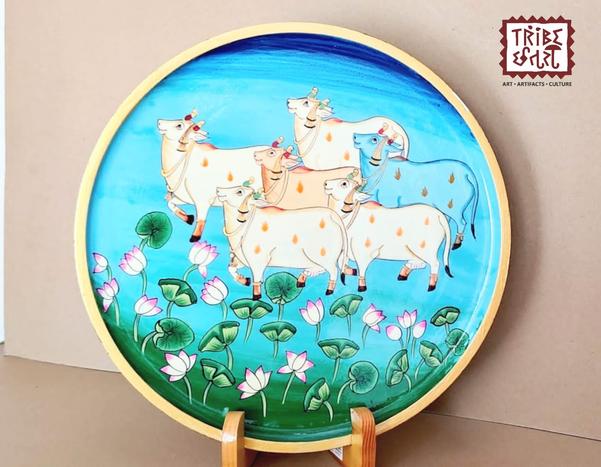 Wooden painted Pichwai platePichwai art wooden plates are exquisite hand-painted pieces that bring the rich heritage of Indian artistry into your living spaces. Originating from Nathdwara, Rajasthan, Pichwai paintings traditionally depict tales of Lord Krishna, often featuring motifs like cows, lotuses, and peacocks. These wooden plates serve as unique wall decor items, blending cultural significance with aesthetic appeal.This piece showcases traditional Rajasthani artistry with intricate cow and lotus motifs, ideal for adding a cultural touch to your decor.Tribe Chatari offers a beautiful collection of wooden hand-painted Pichwai wall plates, blending traditional Indian artistry with contemporary home décor.Size--12
