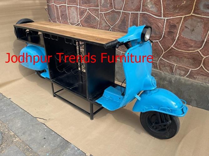 Jodhpur Trends in Jodhpur offers “Reclaimed Wood Scooter Tables”, available in various colors (potentially including blue), emphasizing easy assembly and stylish design . Crafted from durable metal with a solid wooden top and rubber Tyre accents. Finished in blue and black, this piece stands at approximately 108 cm wide × 70 cm deep × 180 cm tall, and comes fully assembled. A hand-crafted rustic design featuring a distressed blue scooter replica.Includes a natural-finish wooden tabletop, a wine rack for 8 bottles, and open storage underneath.