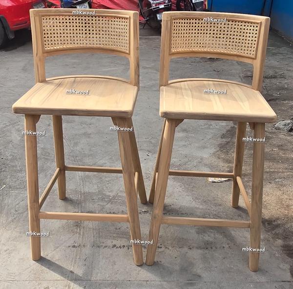 This is a pair of stylish wooden bar stools made by MBK Wood. The stools are crafted from smooth, light-colored wood and feature a comfortable curved seat. The backrest has a beautiful woven cane design, adding both elegance and ventilation. The sturdy wooden legs are supported by horizontal bars, which also serve as footrests. These bar stools are perfect for modern kitchens, cafes, or home bars, offering both comfort and a natural aesthetic.